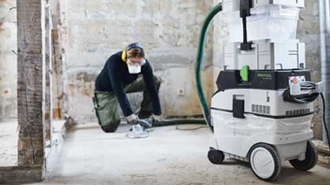 A craftsman is sanding a floor and using the Festool floor sanding system with dust extraction.