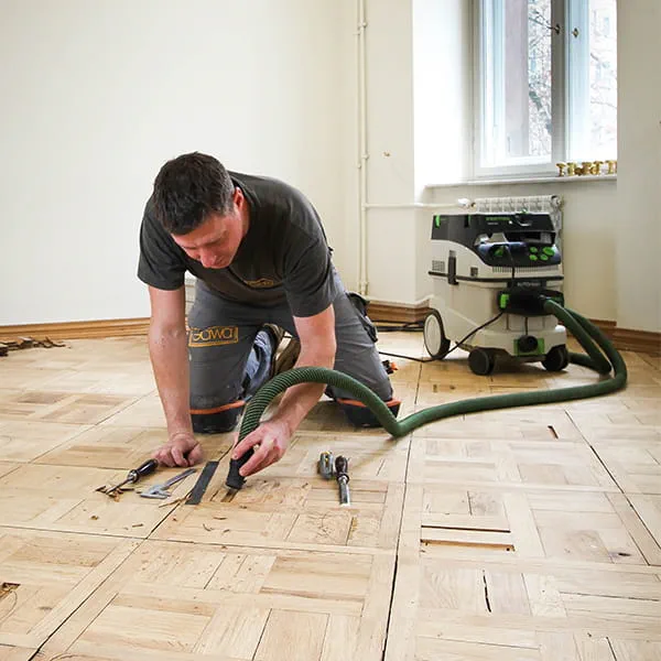 Parquet master installer Jarek Gawina works faulty parts out of the parquet flooring and removes them with the Festool mobile dust extractor