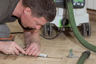 With precision and patience, Jarek, bending low over the parquet, removes unevennesses using a chisel